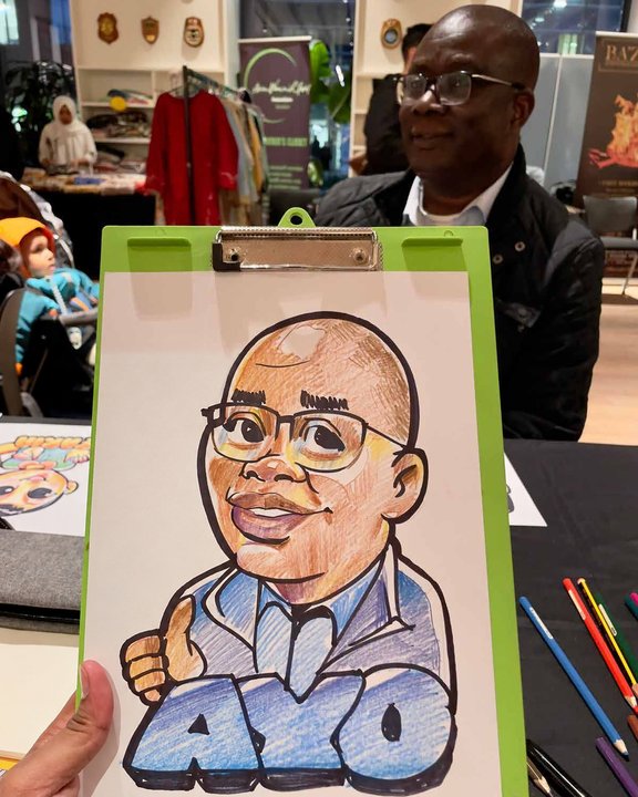 Smiling guest in glasses holding up his colour caricature at a festival market