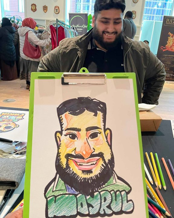 Bearded guest smiling behind his colour caricature at a market event